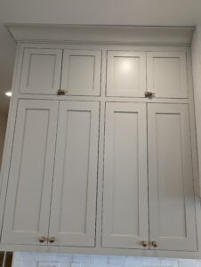 Tall, light gray kitchen cabinets with four lower doors and two upper doors. The upper doors are secured with two clamps. The cabinets have gold knobs and a simple, modern design.